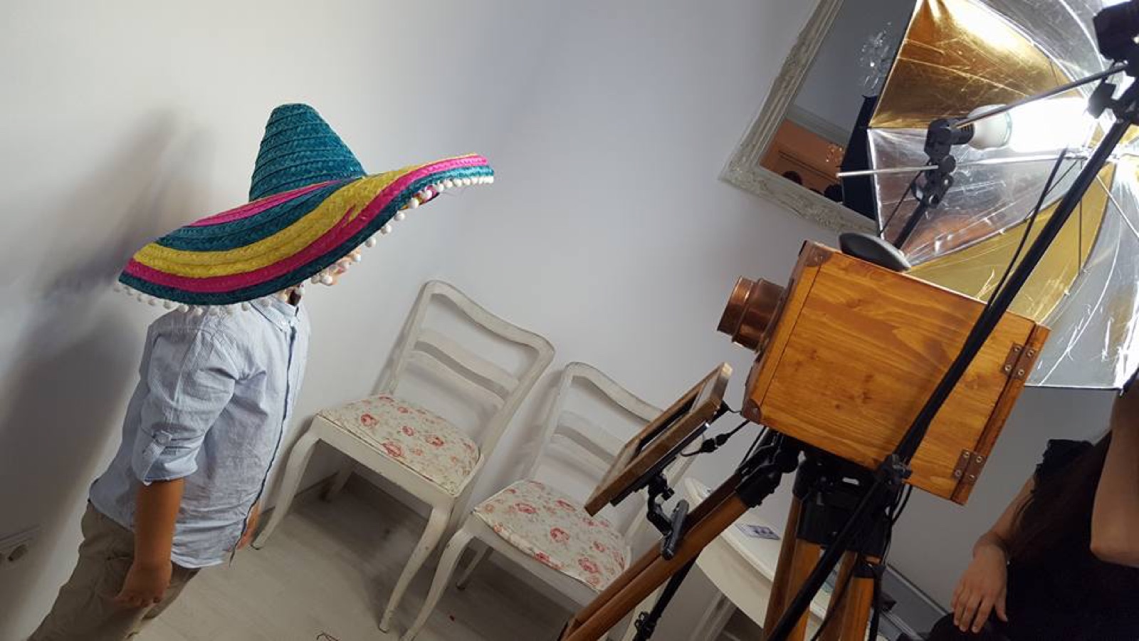 Invitat cu sombrero colorat pozând în fața cabinei foto din lemn, sub lumini de studio